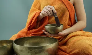 "a person in orange robes using sound bowls to meditate"