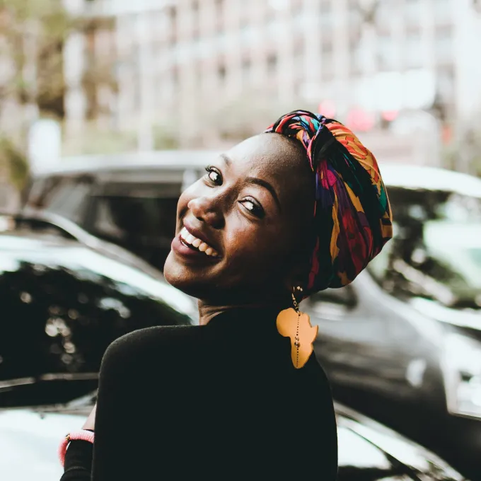 "a, smiling black female wearing an earring shaped like Africa"